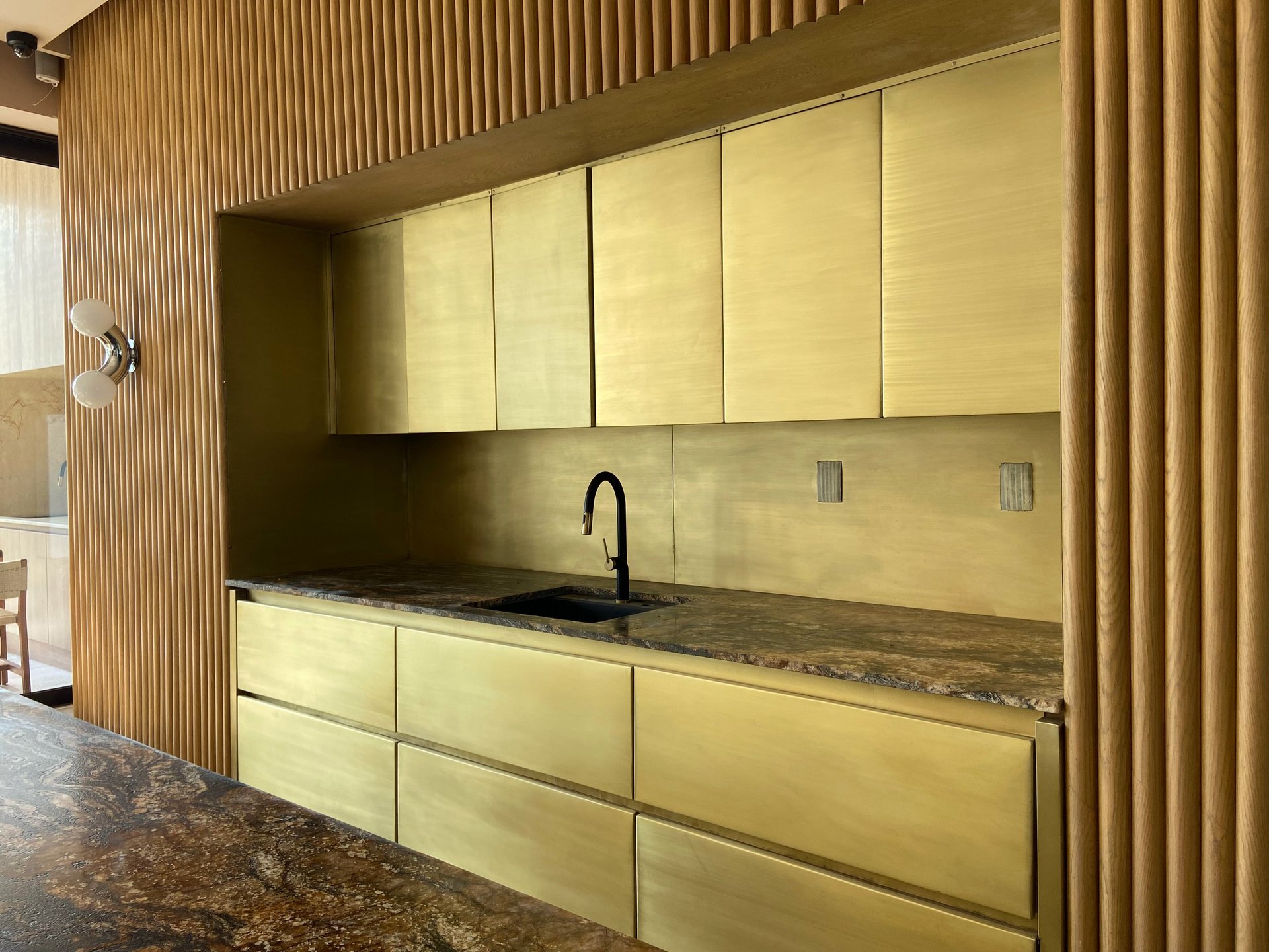 Modern kitchen with pale yellow cabinetry, dark countertop, black faucet, and vertical wood slat wall paneling