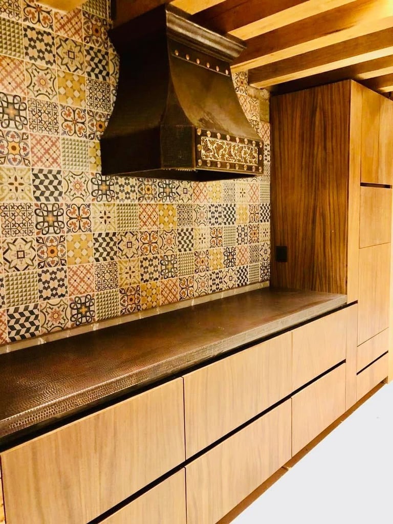 Modern kitchen with patterned tile backsplash, black range hood, light wood cabinetry, and dark countertop