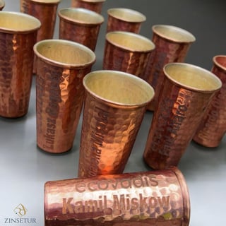 Collection of handcrafted copper cups with embossed text and brass interiors arranged on a gray surface